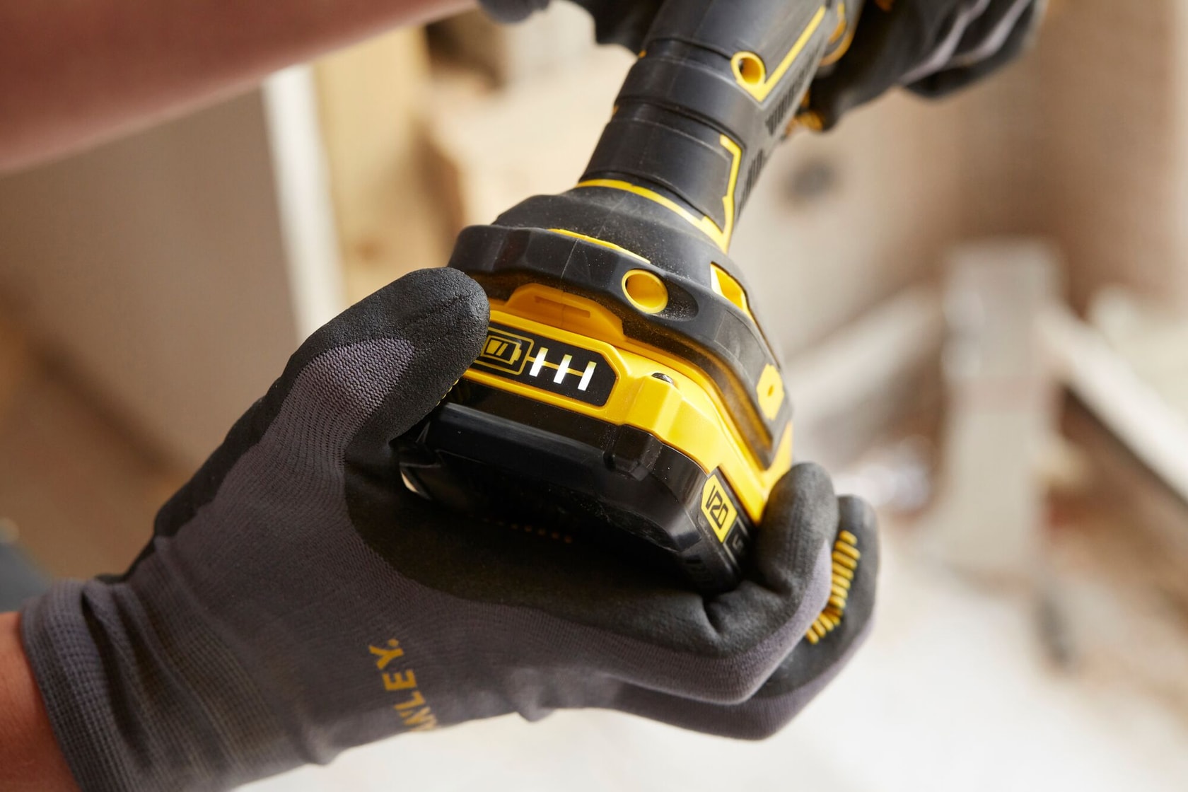 Foto en primer plano de un taladro inalámbrico STANLEY SCD700C2K-B3 sostenido con guantes mostrando el indicador de batería.